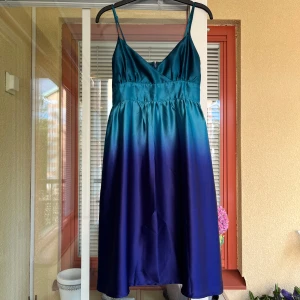 klänning från Soaked in Luxury - Säljer en superfin klänning från Soaked in Luxury. Klänningen har en vacker ombre-effekt som går från havsgrönt till blålila och är gjord i ett glansigt satinmaterial. Den har smala reglerbara axelband och en v-ringad hals. Endast använd ett par gånger. Perfekt för fest! 💙💜