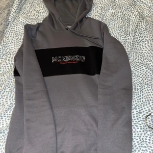 Grå hoodie från McKenzie - Säljer en snygg och bekväm grå hoodie från McKenzie.  Den har en stor ficka på framsidan och en svart detalj med McKenzie-loggan på bröstet. Perfekt för höst och vinter, och passar bra till både vardag och träning. Hoodien är i nyskick och väldigt mjuk och skön att ha på sig. Köp direkt eller ge prisförslag 💛
