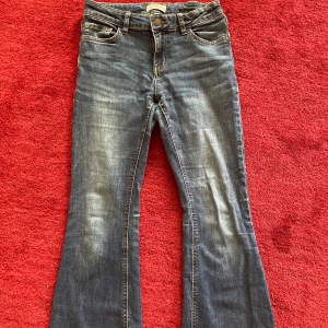 Blå jeans från Lindex - Säljer ett par snygga blå jeans från Lindex. De är i storlek EUR 168 (UK 12-13Y) och har en klassisk femficksdesign. Jeansen har en knapp och dragkedja framtill och är i flare. Perfekta för vardagsbruk!