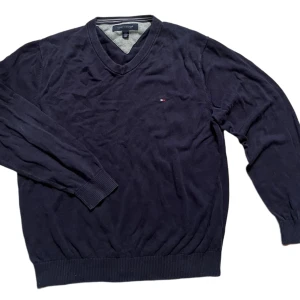 Mörkblå tröja från Tommy Hilfiger - Säljer en stilren mörkblå tröja från Tommy Hilfiger med v-ringning och diskret logga på bröstet. Tröjan har långa ärmar och ribbade muddar vid ärmslut och nederkant. Perfekt för en klassisk look.
