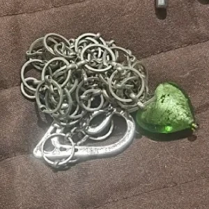 Silverfärgat halsband med grönt hjärthänge - Unikt silverfärgat halsband med ett grönt hjärthänge. Kedjan består av flera sammanlänkade ringar som ger ett elegant och iögonfallande utseende. Perfekt för att ge en färgklick till din outfit.