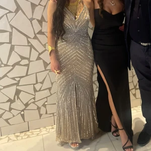 Glittrig långklänning i silver - Elegant glittrig långklänning i silver med djup v-ringning och smala axelband. Perfekt för festliga tillfällen med sin glamorösa design och figurnära passform. Använt endast en gång