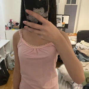 Rosa linnetopp från Joy - Söt rosa linnetopp från Joy med spetsdetaljer vid halsringningen och axelbanden. Perfekt för varma dagar eller som ett lager under andra plagg. Storlek S (36/38).