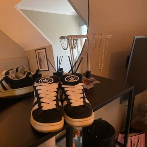 Svarta Adidas Campus sneakers - Snygga svarta Adidas Campus sneakers med vita ränder och snörning. Säljs utan box då den var helt trasig när jag fick hem dem. De har ett hål i hälen