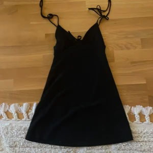 Svart klänning med snörning - Snygg svart klänning med smala axelband och snörning framtill. Perfekt för en stilren look. Klänningen har en enkel design som gör den lätt att matcha med olika accessoarer.