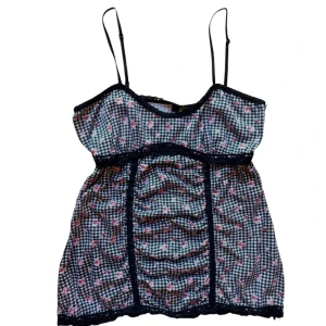 Blommig y2k linne från Bay - Söt linne med smala axelband från Bay. Svart och vit rutig med små rosa blommor och spetsdetaljer. Perfekt för en somrig look! Passar en XS-S. 