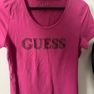 Rosa t-shirt från Guess - Snygg rosa t-shirt från Guess med glittrande logotyp framtill.  Använd någon gång, har inga defekter och alla stenar på trycket finns. Jätte fin t-shirt till sommaren, finns inte längre att köpa