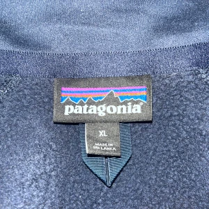 Mörkblå fleecejacka från Patagonia - Säljer en mörkblå fleecejacka från Patagonia i storlek XL dam storlek men passar en kille som har M/L. Jackan har en dragkedja framtill och en praktisk ficka med dragkedja på ärmen. Perfekt för kyliga dagar.
