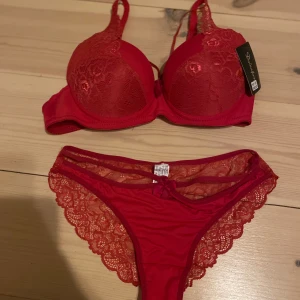 Röd spets-bh och trosor från Laingfang - Snyggt rött underklädesset med spetsdetaljer. Bh:n har justerbara axelband. Trosorna är också i spets med en liten rosett framtill. Storlek S/M.