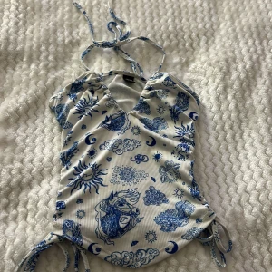 Vit och blå linne topp från Shein - Snygg vit och blått linne från Shein med unikt mönster av sol, måne och moln. Den har knytband i nacken och sidorna för justerbar passform. 