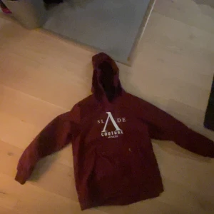 Vinröd hoodie från Slade Couture - Säljer en snygg vinröd hoodie från Slade Couture med tryck på framsidan. Jacka har en praktisk dragkedja på ärmen för att ha liftkort i och en bekväm huva. Perfekt för en avslappnad stil i backen 