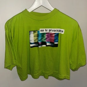 Grön croppad t-shirt med tryck - Snygg grön croppad t-shirt med ett färgglatt tryck och texten 'no te preocupes' (don’t worry på spanska). Perfekt för en avslappnad stil.