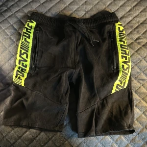 Svarta shorts med neongula detaljer - Snygga svarta shorts med neongula detaljer . De har dragkedjor på sidorna och en elastisk midja för bekväm passform. Perfekta för en sportig look! Vet inte vart jag har köpt dom eller något och har tyvärr klippt av taggarna.