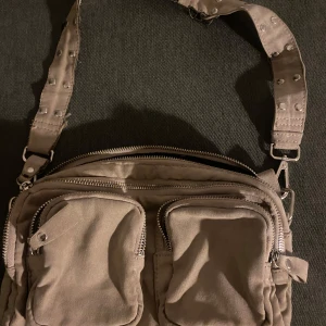 Nunoo inspirerad väska i beige  - En nunoo inspirerad väska i beige mocka imitation från Gina tricot i perfekt storlek för vardagsgrejer som ska med i farten. Kan bäras på axeln och korsad.  Bild på defekten på sida 2 