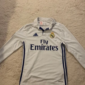 Real Madrid hemma 2016/17 - Real Madrid tröja från 2016/17 säsongen, långärmad och riktigt fet. Den är dock ganska gammal då trycket har börjat ramla av och real Madrid loggan fick klistras tillbaka därav priset. Det är största barnstorelken men passsar xs-s