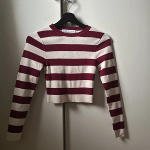 Randig croppad tröja från Zara - Säljer en  randig tröja från Zara i vinrött och vitt. Tröjan är croppad med långa ärmar och har en ribbad rund halsringning. Perfekt för en trendig look!. Kan vara lite kortare på
