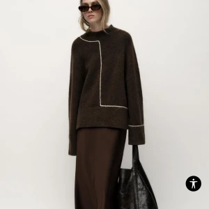 Brun stickad tröja med vita detaljer - Snygg brun stickad tröja med unika vita linjedetaljer. Tröjan har en avslappnad passform. Tröjan är nu endast använd 1 gång.