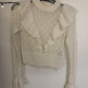 Vit stickad tröja med volangdetaljer - Superfin hål stickad tröja med volanger och vida armar som tyvärr inte kommer till. Använd max 5 gånger och inget fel på den. Skriv för fler bilder så löser jag💖 (Tröjan är mer vit i verkligheten)