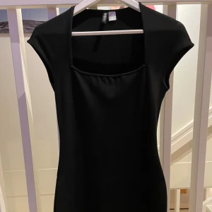 Svart klänning från H&M - Andvänd 1 gång. Elegant svart klänning från H&M med en stilren design. Klänningen har en tight passform och korta ärmar, vilket ger en sofistikerad look. Perfekt för en kväll ute eller en speciell tillställning.