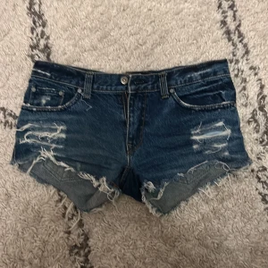 Blå jeansshorts med slitningar - Lågmidjade coola blå jeansshorts med slitna detaljer och fransiga kanter. Fina detaljer på fickorna