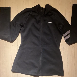 Svart träningsjacka från Stronger - Snygg svart träningsjacka från Stronger med dragkedja och coola vita detaljer på ärmarna. Perfekt för träning eller en aktiv vardag.