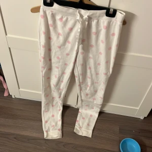 Vita mjukisbyxor med rosa prickar från Kappahl  - Mysiga vita mjukisbyxor från Kappahl med söta rosa prickar. Byxorna har en bekväm passform och ett knytband i midjan för justerbarhet. Perfekta för en avslappnad dag hemma.