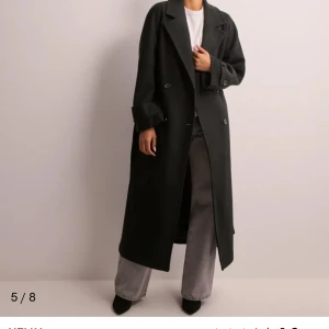 Svart kappa med bälte - Elegant svart kappa med knappar och bälte i midjan. Långärmad design med klassisk krage och stilren look. Perfekt för kyligare dagar. Knappt använd, som ny. Stor i storleken, jag är vanligtvis en S, men XSS passar mig i kappan.