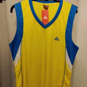 Helt ny Gul och blå ärmlös topp från Lidong - Snygg gul och blå ärmlös topp från Lidong. Perfekt för sportiga aktiviteter med sin lätta och luftiga design. Den har en v-ringad hals och kontrasterande blå detaljer vid ärmhålen och halsen. Helt ny och är oanvänd!
