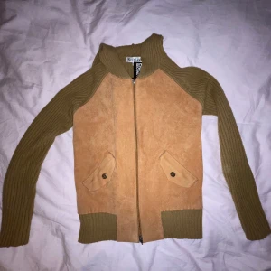 Beige och brun hoodie med dragkedja - Snygg hoodie i beige mocka och brunt ribbat material. Tröjan har en dragkedja framtill och praktiska fickor med knappar. Perfekt för en stilren och bekväm look.