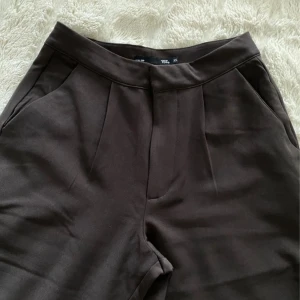 Bruna byxor från 157 - Snygga bruna byxor från 157 i storlek XS. Byxorna har en hög midja och vida ben, vilket ger en modern och bekväm passform. Perfekta för en stilren look.