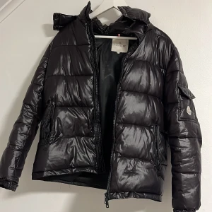 Svart dunjacka från Moncler - Snygg svart dunjacka från Moncler med glansig finish. Jackan har en dragkedja framtill och praktiska fickor med dragkedjor. Den har en klassisk pufferdesign och en liten logotyp på ärmen. Perfekt för kyliga dagar. Pris kan diskuteras ifall du är fundersam kan sänka om de är en. snabb affär Storlek S passar också M