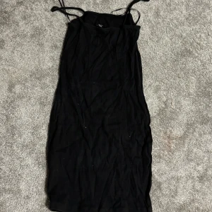 Svart axelbandslös klänning - Elegant svart axelbandslös klänning med smala axelband. Perfekt för en stilren look.