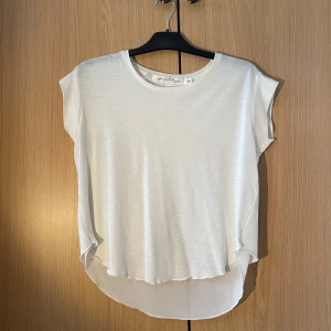 Vit omlottopp med broderade vingar - Säljer en stilren vit omlottopp från Grobz i storlek S. Toppen har korta ärmar och ett vackert broderi av vingar på sidan. Perfekt för en avslappnad och chic look.