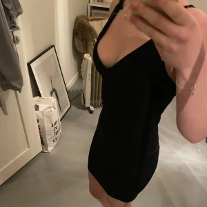 Svart klänning från Boohoo - Snygg svart klänning från Boohoo med smala axelband och djup v-ringning. Klänningen har en åtsittande passform och snörning i ryggen för en extra detalj. Perfekt för en utekväll eller festlig tillställning.