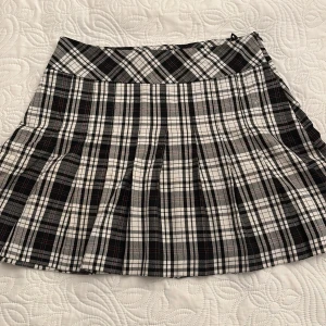 Rutig kjol från Lindex - Snygg rutig kjol från Lindex i svart, vit och grå. Kjolen har ett klassiskt rutmönster och är tillverkad i en blandning av polyester och viskos. Den har en dragkedja i sidan för enkel på- och avtagning. Längd ungefär vid mitten av låren! 