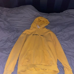Gul hoodie med tryck - Säljer en gul hoodie med tryck på bröstet. Den har en klassisk känguruficka och en bekväm huva med dragsko. Perfekt för en avslappnad stil.