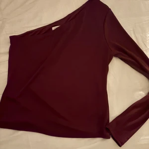 Vinröd oneshoulder topp - Snygg vinröd oneshoulder topp från Stockh LM Studio. Perfekt för en stilren look med sin eleganta design och långa ärm. Passar utmärkt till både jeans och kjol.💞💞