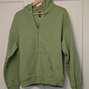 Grön hoodie från H&M - Säljer en grön hoodie från H&M med dragkedja och huva. Tröjan har långa ärmar och en praktisk ficka framtill. Köptes på plick för 130, inte användts sen dess