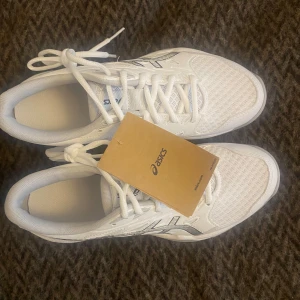 Vita Asics Gel-Rocket 11 - Säljer ett par vita Asics Gel-Rocket 11 med silverdetaljer. Perfekta för inomhussporter med bra grepp och komfort. Skorna har snörning och en stilren design. De är helt oanvända och lådan har endast öppnats.