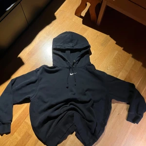 Svart hoodie från Nike, Center swoosh - Säljer en klassisk svart hoodie från Nike med vit center swoosh. Tröjan har en justerbar huva med dragsko och långa ärmar. Perfekt för en avslappnad stil. Storlek Small och bra skick då den inte blivit använd 