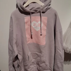 (Intressekoll) K-12 hoodie - En ljuslila hoodie med rosa Melanie Martinez tryck på. Lite nopprig på vissa ställen. Officiell merch.