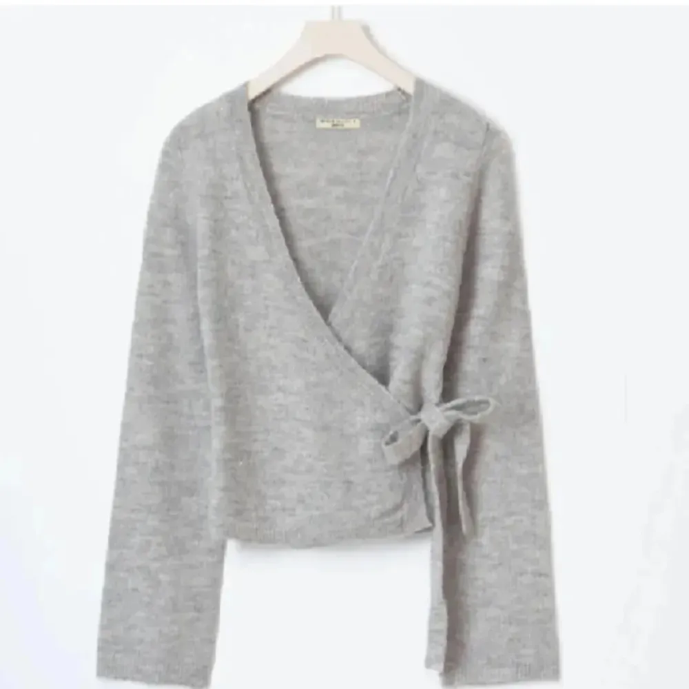 Mysig grå omlottkofta med knyt i sidan. Perfekt för lager-på-lager och ger en avslappnad look. Långärmad design i mjukt material.. Neuletakit & Villapaidat.