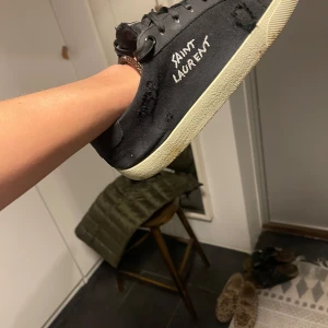 Svarta sneakers från Saint Laurent - Snygga svarta sneakers från Saint Laurent med vit sula och logotyp på sidan. Skorna har snörning och en stilren design som passar perfekt för en trendig look. 