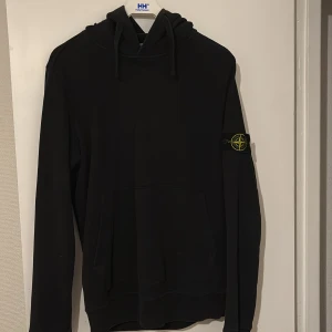 Svart hoodie från Stone Island - Säljer en stilren svart hoodie från Stone Island med det ikoniska märket på ärmen. Perfekt för en casual look med en skön passform och justerbar huva.