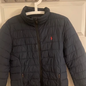 Mörkblå quiltad jacka från Polo Ralph Lauren - Säljer en mörkblå quiltad jacka från Polo Ralph Lauren med dragkedja och broderad logga på bröstet. Perfekt för kyligare dagar med sin stilrena design och bekväma passform.storlek L,14-16( barn storlek) ca xs-s