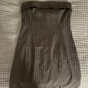 Svart axelbandslös klänning med ränder - Snygg svart axelbandslös klänning med vita tänder. Klänningen har en tubformad design och är i storlek M. Säljer då den är för stor. Aldrig använd med prislapp, köpt för 499🫶