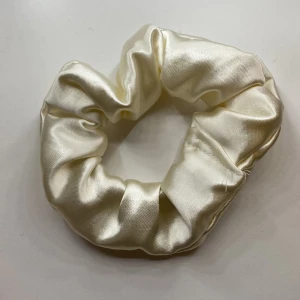 Vit scrunchie i satin - Elegant vit scrunchie i satin som ger en lyxig känsla. Perfekt för att sätta upp håret med stil eller som en snygg accessoar runt handleden. Freebies kommer även med!
