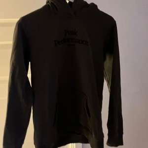 Mörk grå hoodie från Peak Performance - Säljer en mörk grå hoodie från Peak Performance med tryck på bröstet. Den har en klassisk design med huva och långa ärmar. Pris kan diskuteras.