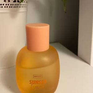 Sunset Lover parfym från Sence - En elegant parfymflaska med en mjuk, matt orange ton och en ljusrosa kork. Doften heter 'Sunset Lover' och ger en känsla av varma sommarkvällar. Perfekt för den som vill ha en fräsch och ungdomlig doft.💞