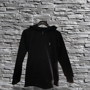 Svart hoodie från Ralph Lauren - Snygg svart hoodie från Ralph Lauren med dragkedja och klassisk logga på bröstet. Perfekt för en avslappnad stil med långa ärmar och huva.